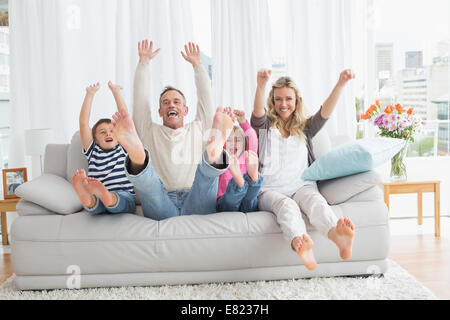 Family sitting on a couch et raising arms Banque D'Images