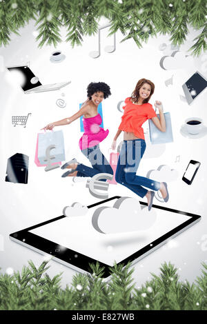 Image composite de deux smiling women jumping on a tablet pc Banque D'Images