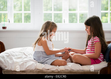 Deux filles sitting cross legged en face de l'autre, tenant un téléphone intelligent. Banque D'Images