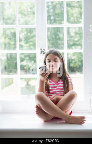 Une fille assise jouant, tenant un téléphone intelligent. Banque D'Images