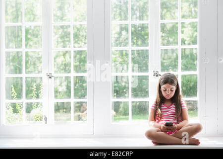 Une fille assise jouant, tenant un téléphone intelligent. Banque D'Images