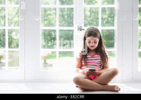 Une fille assise jouant, tenant un téléphone intelligent. Banque D'Images