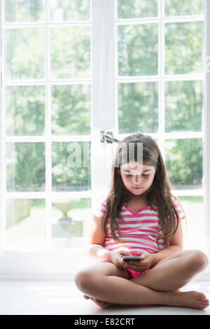 Une fille assise jouant, tenant un téléphone intelligent. Banque D'Images