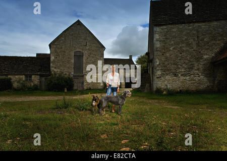 Une femme debout dans l'ombre dans une basse-cour avec deux gros chiens lurcher. Banque D'Images