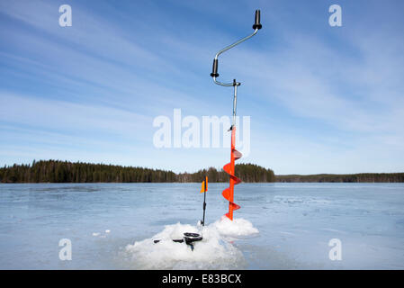 Mangeoire à glace à main et canne de pêche à glace à la pointe vers le haut au lac gelé à Winter, Finlande Banque D'Images