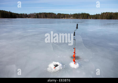 Mangeoire à glace à main et canne de pêche à glace à la pointe vers le haut au lac gelé à Winter, Finlande Banque D'Images