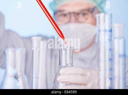 Les scientifiques des gouttes d'un liquide rouge d'une pipette dans un flacon en verre. Banque D'Images