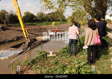 Burrowbridge, Somerset, Royaume-Uni. 30 Septembre, 2014. Une équipe de télévision international media watch que le dragage se poursuit le long de la rivière Parrett sur Somerset Levels. Du limon aujourd'hui de la mi channel de la Parrett est transférée par une barge de déchargement avant sur le tracteur et remorques pour l'épandage sur les champs. Banque D'Images