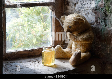 Un ours en peluche aux yeux élimés sur un rebord de fenêtre à l'ancienne à la recherche d'un pot de miel Banque D'Images