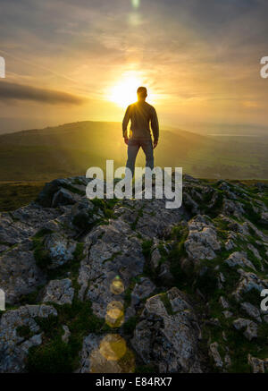 Une figure solitaire regardant le lever du soleil depuis le sommet d'une colline. Banque D'Images