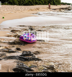 Un bateau en plastique gonflables enfant flotte librement sur une plage tropicale à Sainte Croix, îles Vierges américaines. Une femme en arrière-plan. Banque D'Images