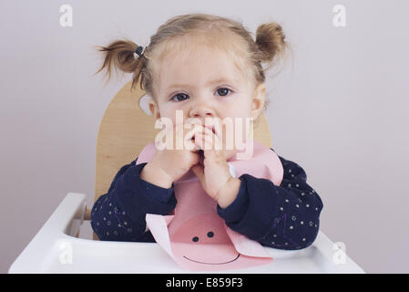 Baby Girl sitting dans une chaise haute, à mâcher sur les doigts Banque D'Images