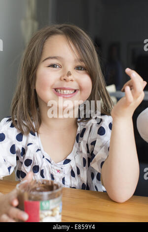 Little girl eating chocolate sauce de un pot avec ses doigts Banque D'Images