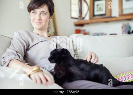Woman relaxing on sofa avec chat sur ses genoux Banque D'Images