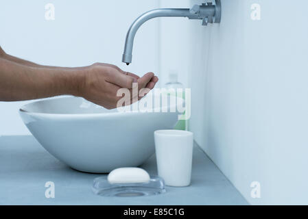 Homme tenant les mains à robinet d'égoutture dans salle de bains lavabo, cropped Banque D'Images