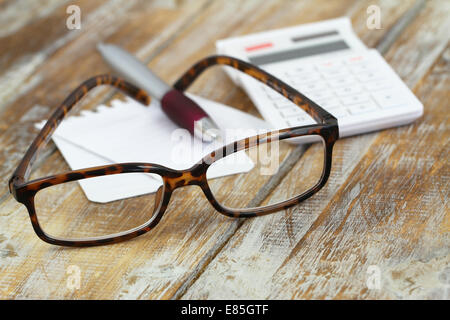 Lunettes de lecture, calculatrice, stylo et note sur la surface en bois Banque D'Images