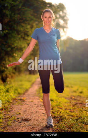 Jeune femme faisant des exercices d'étirement comme elle limbers up ses muscles pour aller sur un jogging ou commencer un entraînement debout sur un pays Banque D'Images