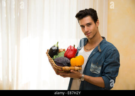 Jeune homme tenant un panier de légumes frais contenant une aubergine, poivrons doux et le chou dans un plat végétarien ou la santé Banque D'Images