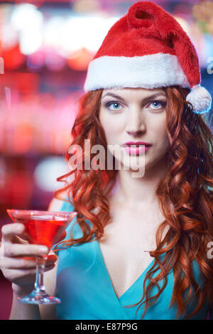 Fille à tête rouge à Santa cap avec verre de martini looking at camera Banque D'Images