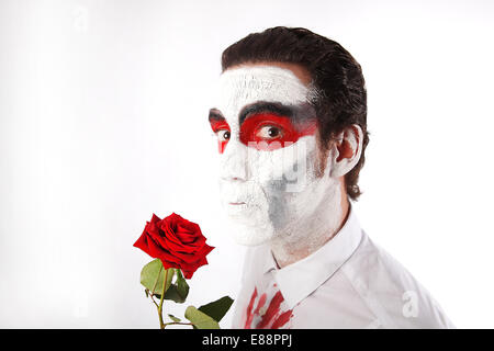 L'homme blanc avec mascara et bloody shirt détient rose rouge devant un fond blanc Banque D'Images