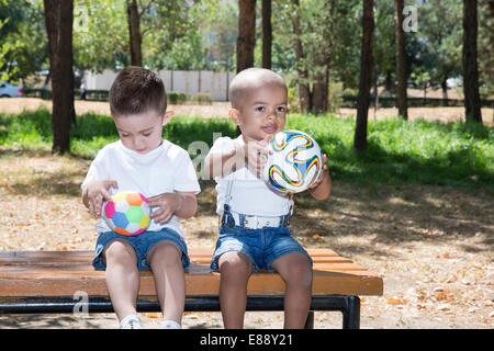 Petits garçons : African American et caucasienne avec ballon de soccer dans le parc de la nature à l'été. L'utiliser pour bébé et sport concept Banque D'Images