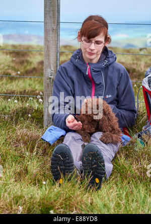 Un female hiker nourrir leur chien tandis que dehors sur une promenade dans la campagne. Banque D'Images