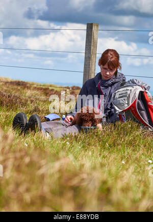 Un female hiker nourrir leur chien tandis que dehors sur une promenade dans la campagne. Banque D'Images