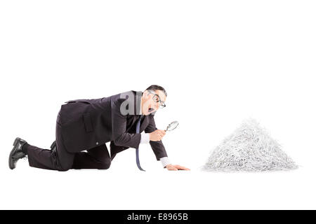 Businessman looking at une pile de papier déchiqueté avec loupe isolé sur fond blanc Banque D'Images