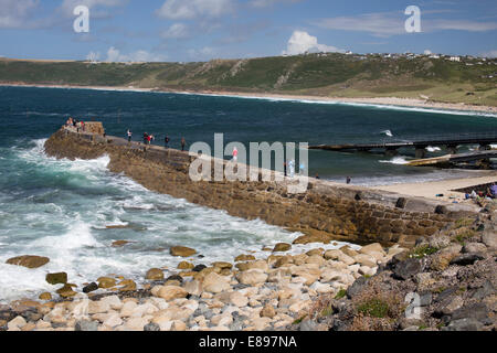 Les personnes bénéficiant de l'beau temps à marcher le long de la digue du port, Sennen Cove, Cornwall, England, UK. Banque D'Images