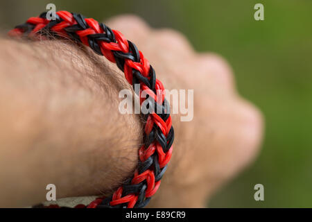 Un bracelet rouge et noir fabriqué à partir de bandes à tisser sur un poignet de l'homme. Parution du modèle. Banque D'Images