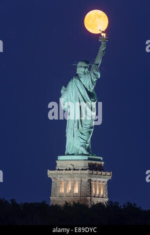 La super pleine lune se lève au-dessus de la Statue de la liberté au cours de l'heure bleue. Banque D'Images