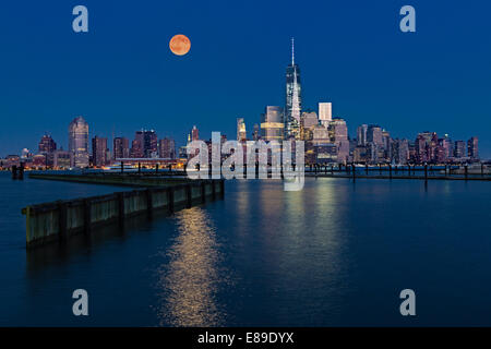La super pleine lune se lève au-dessus de l'allumé de gratte-ciel dans le lower Manhattan skyline le long de One World Trade Center. Banque D'Images