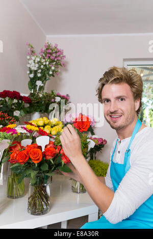 Young Woman arranging flowers in vase, smiling Banque D'Images