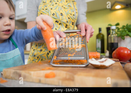 Boy aider sa mère pour râper les carottes dans la cuisine Banque D'Images
