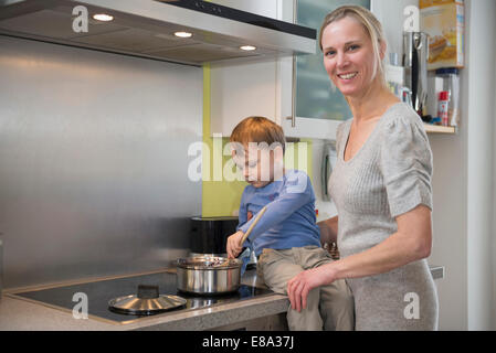 Boy aider sa mère en remuant la nourriture en pot, smiling Banque D'Images