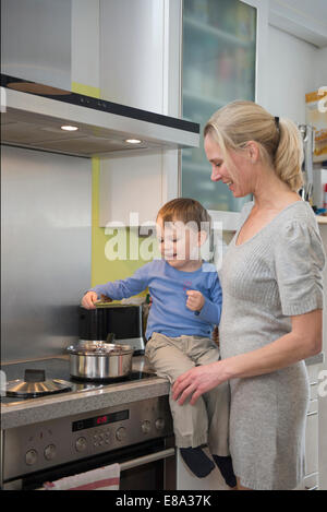 Boy aider sa mère en remuant la nourriture en pot, smiling Banque D'Images