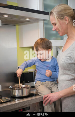 Boy aider sa mère en remuant la nourriture en pot, smiling Banque D'Images