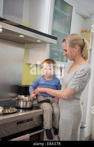 Boy aider sa mère en remuant la nourriture en pot, smiling Banque D'Images