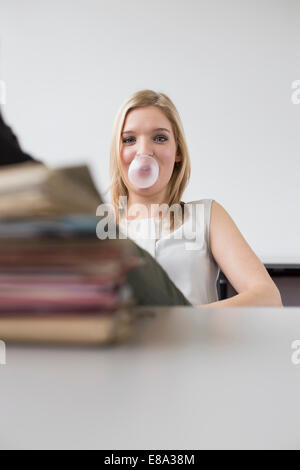 Woman blowing bubble gum in office Banque D'Images