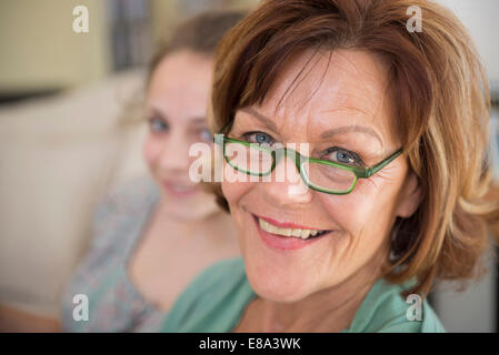 Portrait de grand-mère et petite-fille sitting on couch in living room, smiling Banque D'Images