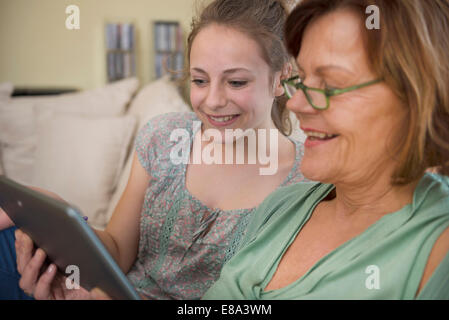 Grand-mère et petite-fille using digital tablet in living room, smiling Banque D'Images