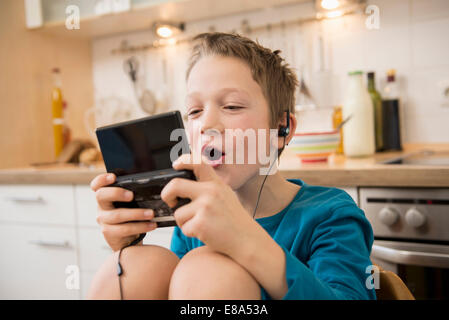 Boy playing video game in kitchen Banque D'Images