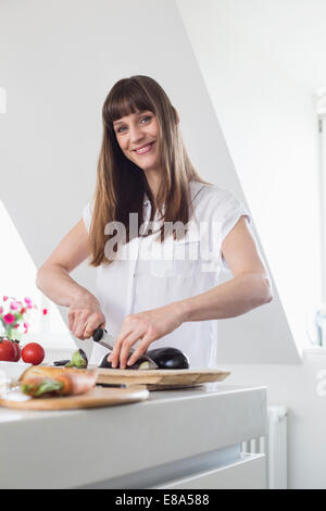 Portrait of mid adult woman cutting aubergine en cuisine, smiling Banque D'Images