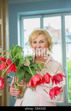 Portrait of mature woman holding vase avec des tulipes, smiling Banque D'Images