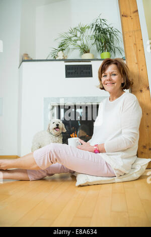 Portrait of senior woman avec chien assis devant le foyer, smiling Banque D'Images