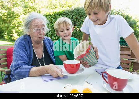 Petit-fils de verser du lait dans son grand-mères tasse Banque D'Images