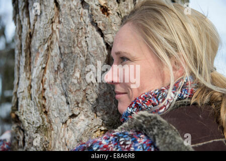 Woman hugging tree trunk, smiling, Bavière, Allemagne Banque D'Images