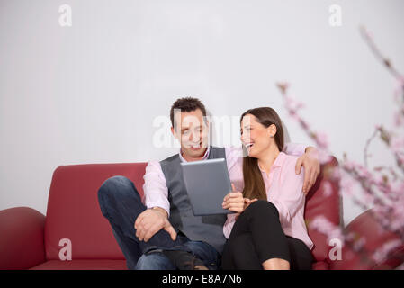 Jeune couple assis canapé rire tablet computer Banque D'Images