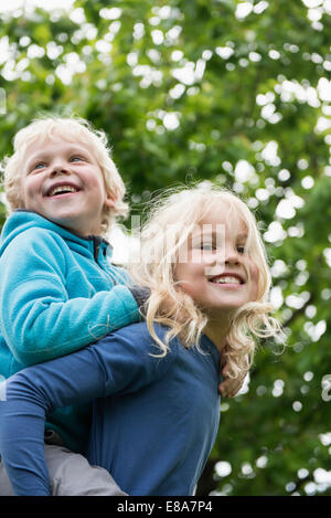 Jeune fille blonde exerçant son frère piggyback Banque D'Images