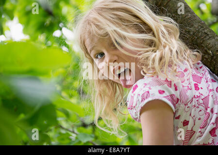 Young Girl sitting in tree sticking tongue out Banque D'Images